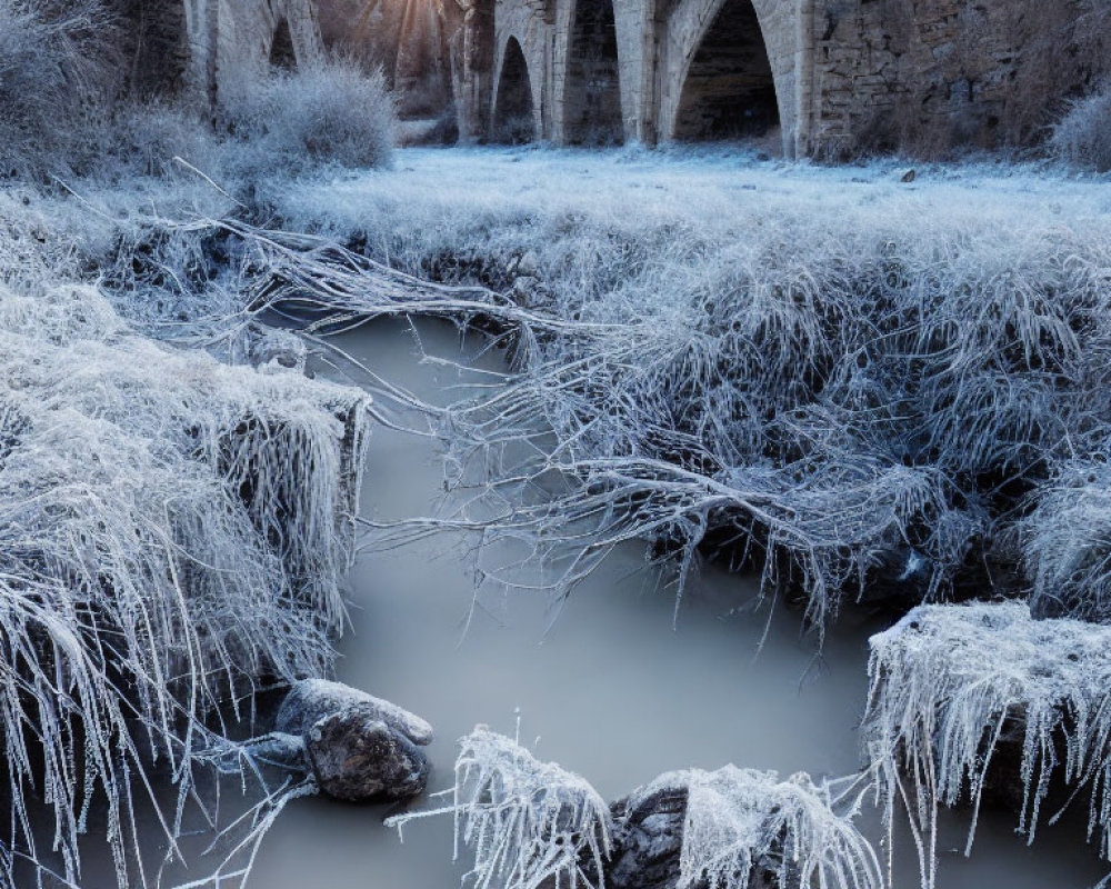 Stone bridge over frosty river with sunbeams and icy landscape