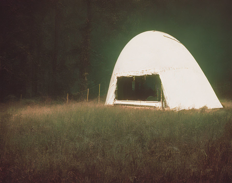 Nighttime camping scene with illuminated dome-shaped tent in dark field
