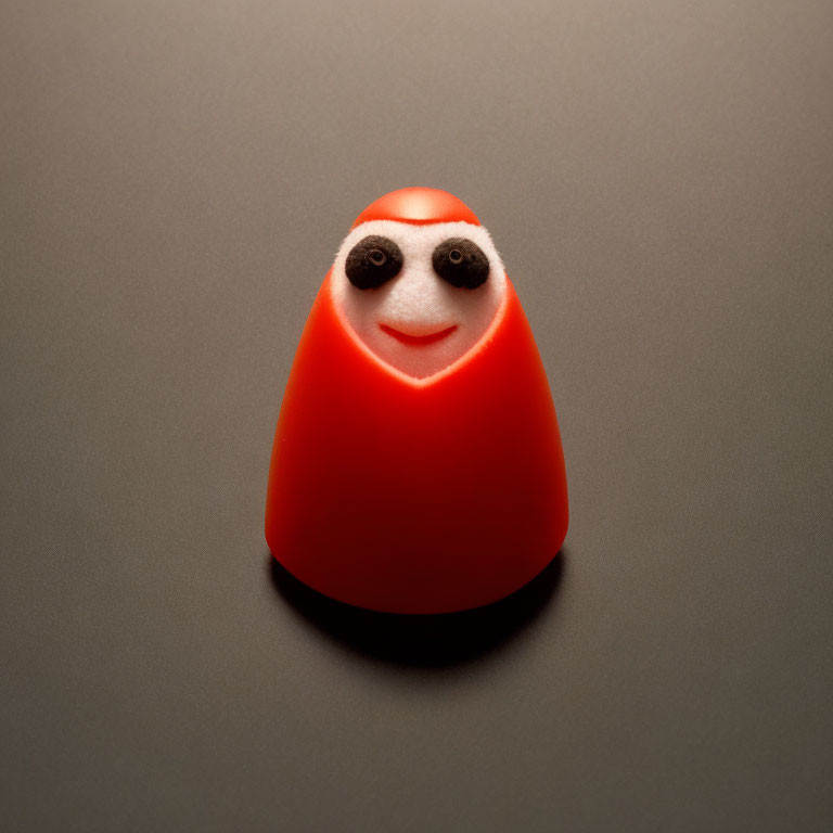 Red Smiling Cone-Shaped Object with Googly Eyes on Grey Background