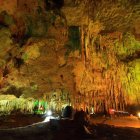 Illuminated underground cave with stalactites, stalagmites, and reflective pool.