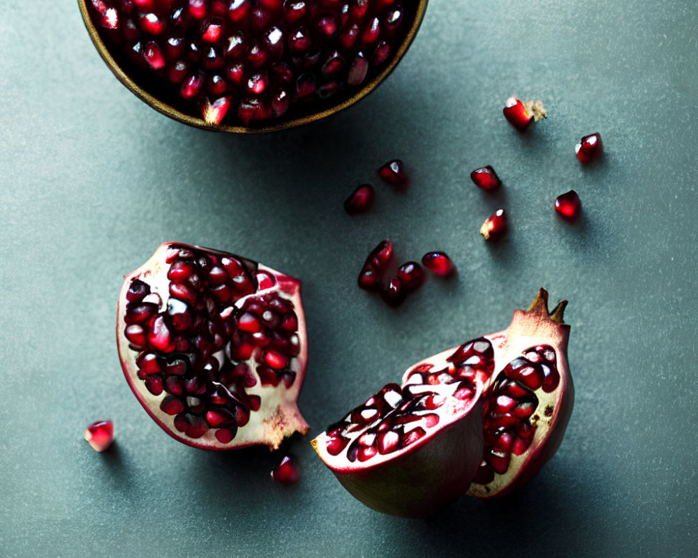 Ripe pomegranate halves and seeds on dark surface, one bowl filled.