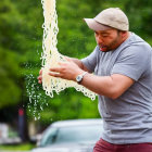 Man in Gray T-Shirt and Cap Spitting Long Noodles Outdoors