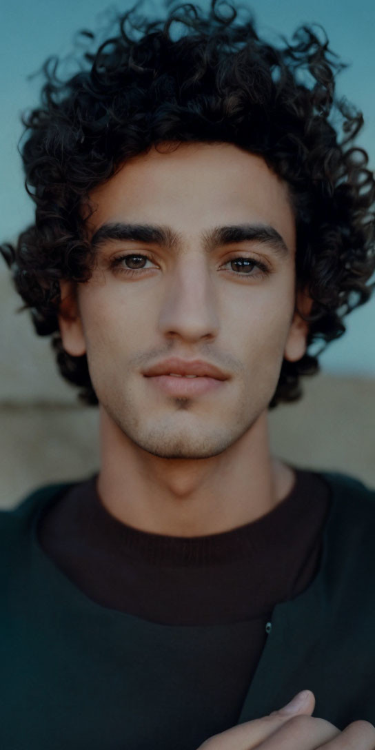 Curly-Haired Man Portrait with Focused Eyes and Green Top