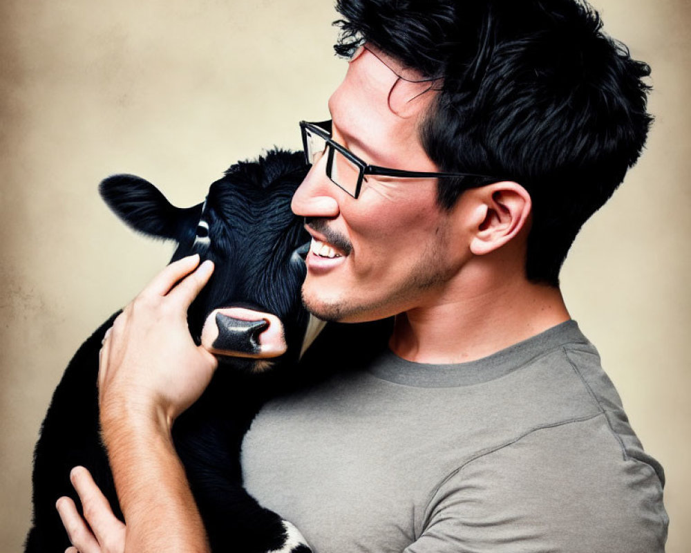 Man smiling with glasses embracing black and white calf on warm backdrop
