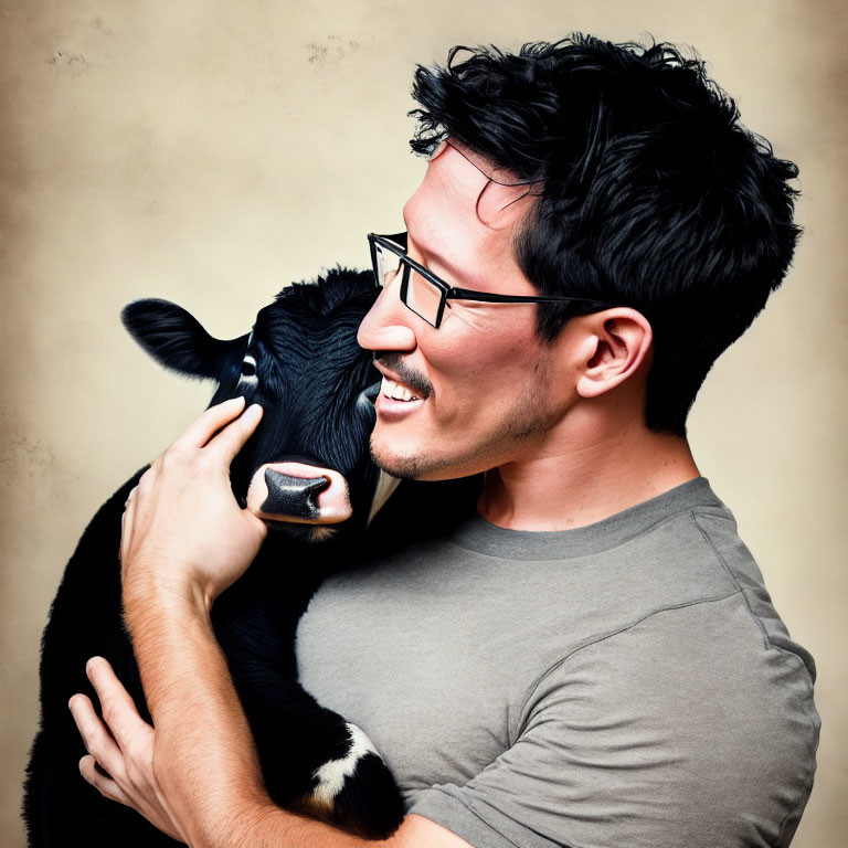 Man smiling with glasses embracing black and white calf on warm backdrop