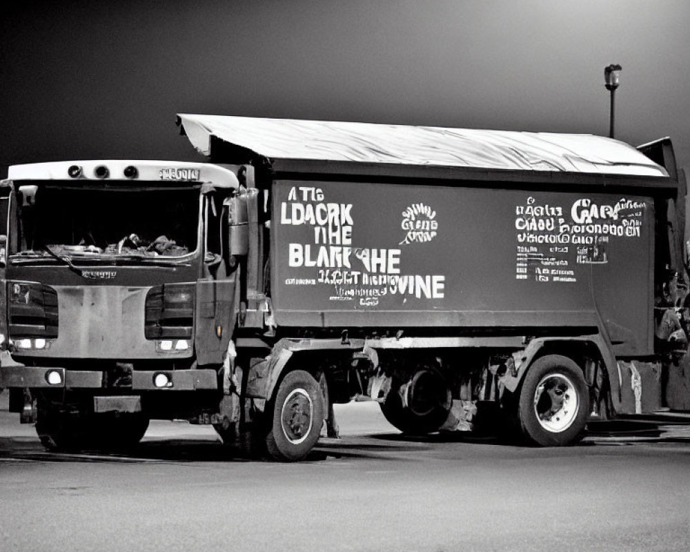 Monochrome image of graffiti-covered garbage truck at night