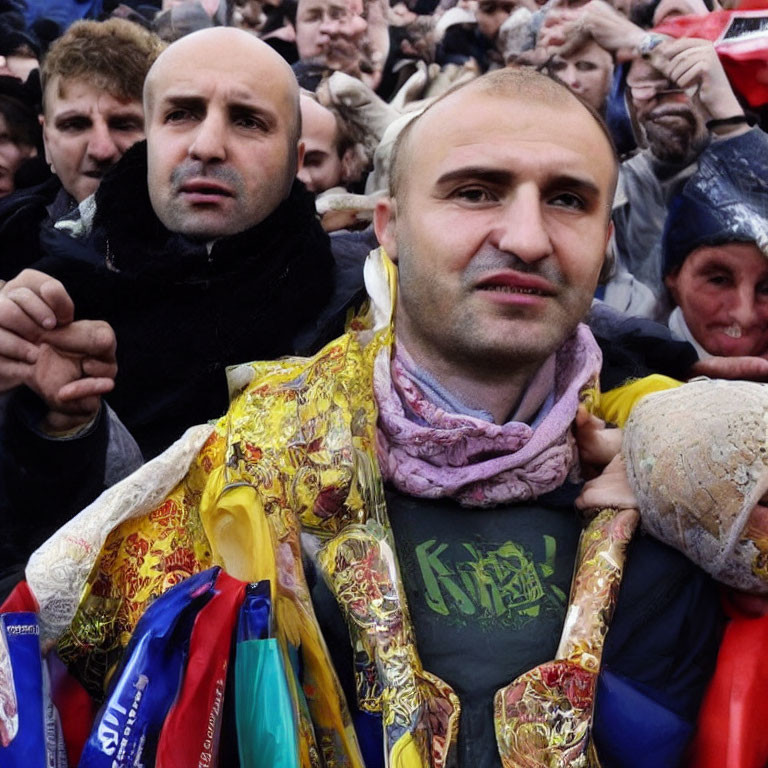 Crowded scene with bald man in scarf and ribbons smiling at camera