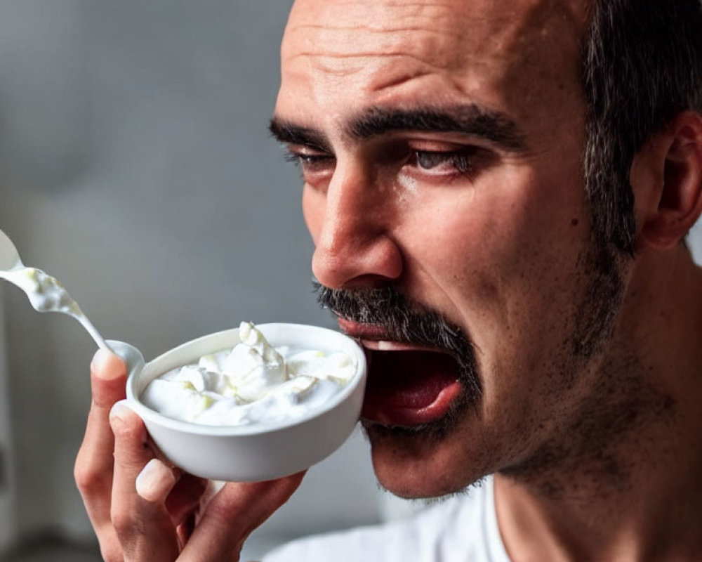 Mustached man eating yogurt with spoon in humorous anticipation