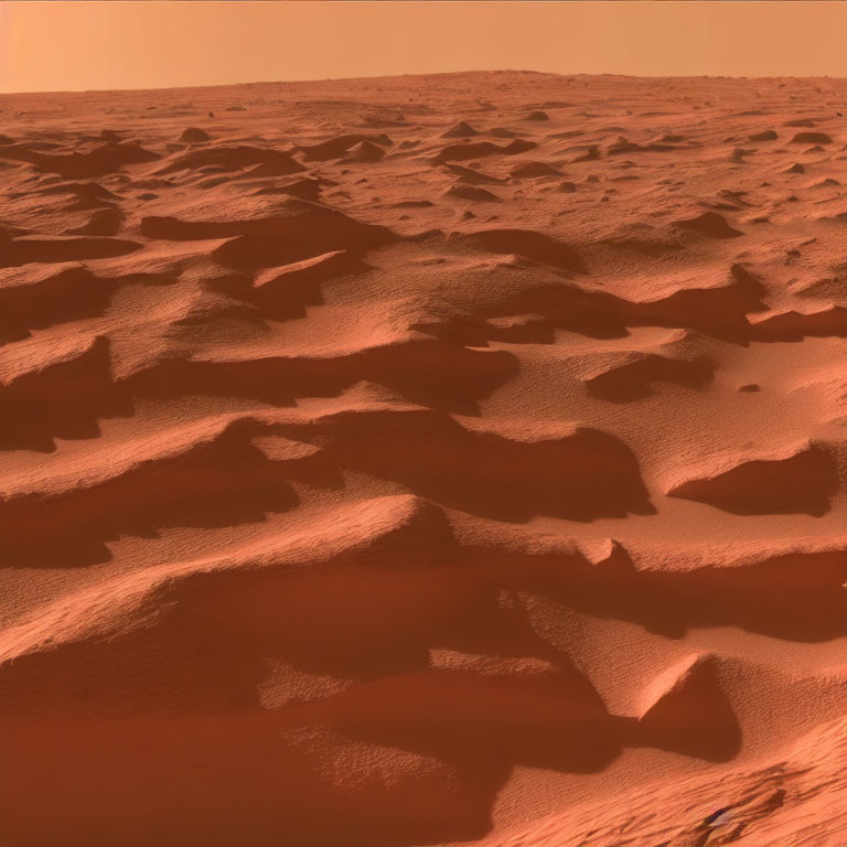 Reddish Martian terrain with windswept dunes under a hazy sky