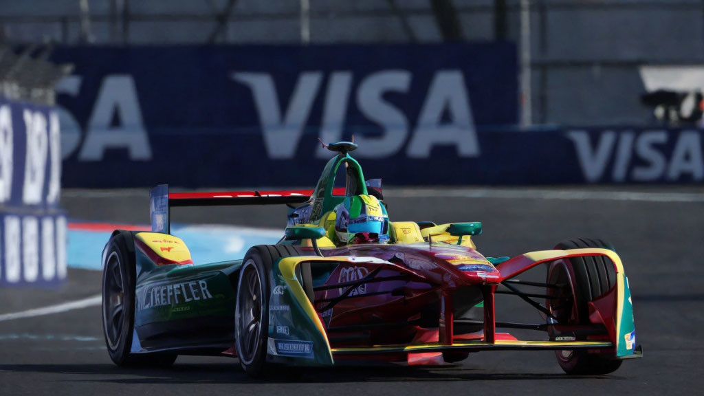 Vibrant Formula E race car on track with tire barriers and sponsorship banners