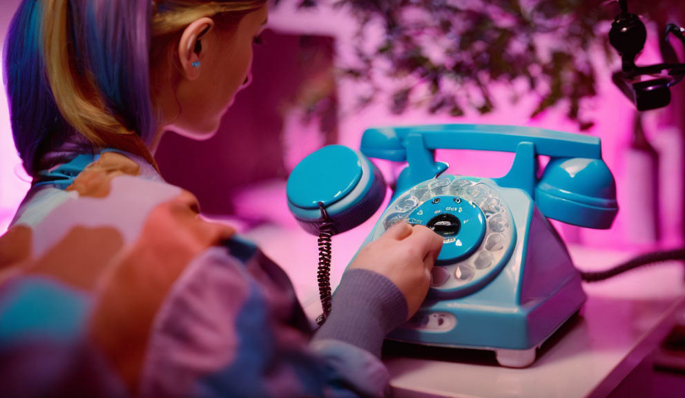 Person dialing vintage rotary phone under pink neon light