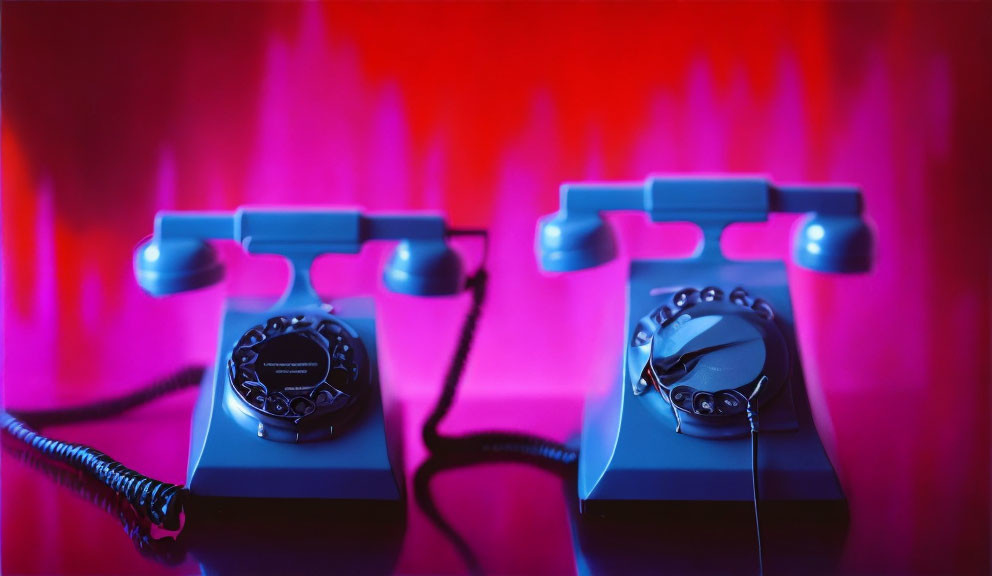 Vintage rotary dial telephones on red and purple backdrop, one with twisted cord.