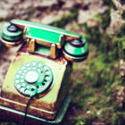 Vintage Green Rotary Phone Covered in Moss Against Blurred Natural Background