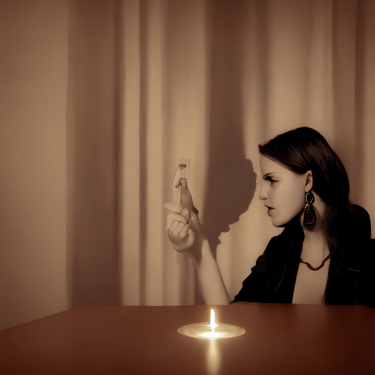 Woman sitting at table with lit candle and extinguished matchstick, casting shadow on draped background.