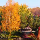 Colorful autumn landscape with bridge, river, and figure in white amidst lush foliage.