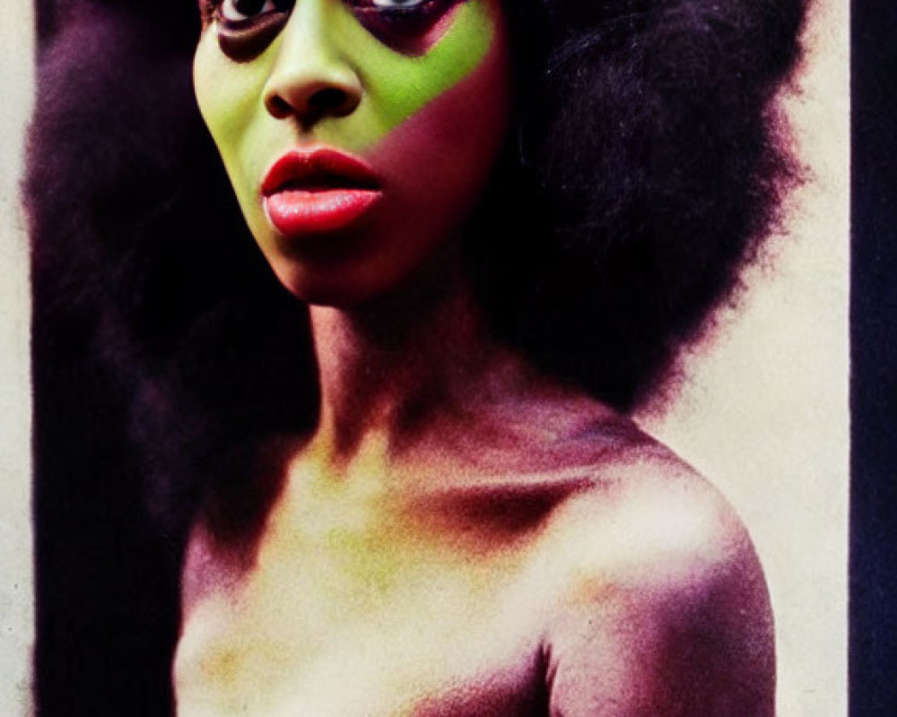 Woman with vibrant green and pink makeup and afro hair against grunge-style backdrop