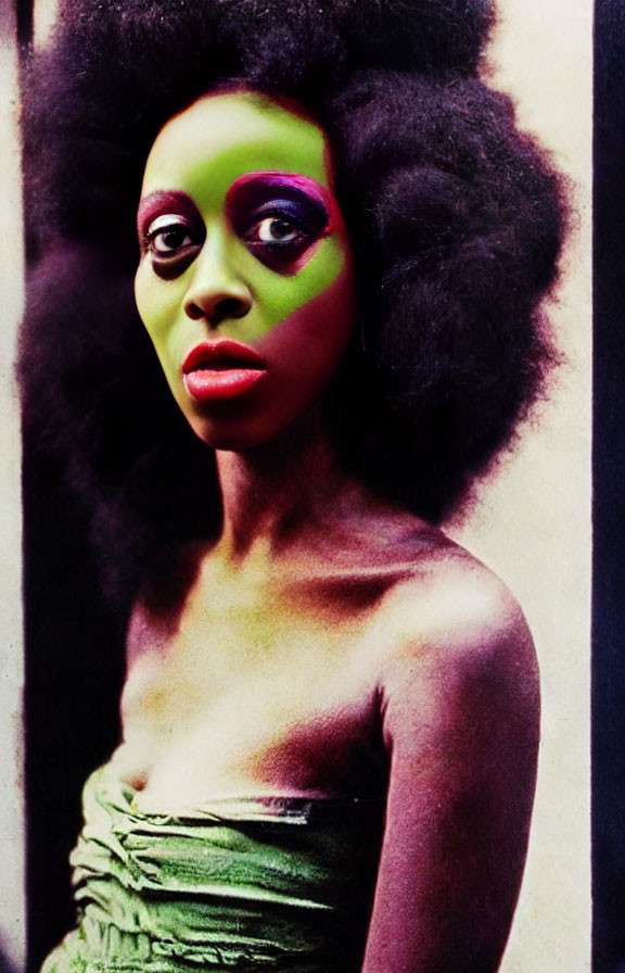 Woman with vibrant green and pink makeup and afro hair against grunge-style backdrop