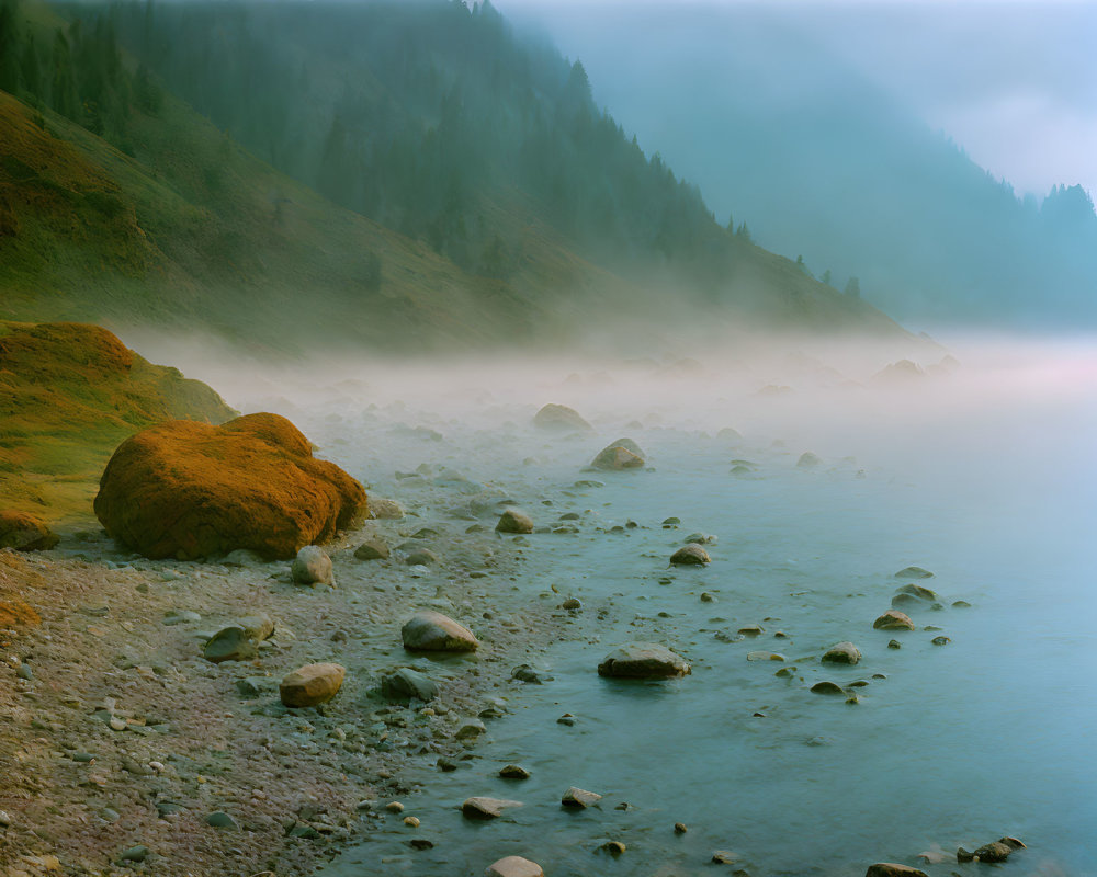 Tranquil lakeside scene with moss-covered boulders and foggy mountain backdrop