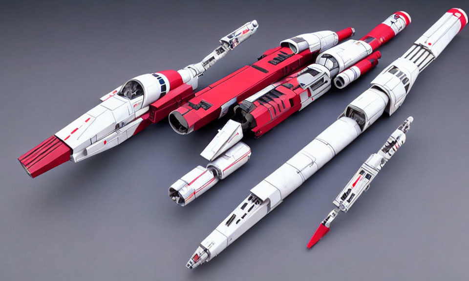 Three miniature spaceship models: red and white designs on grey surface