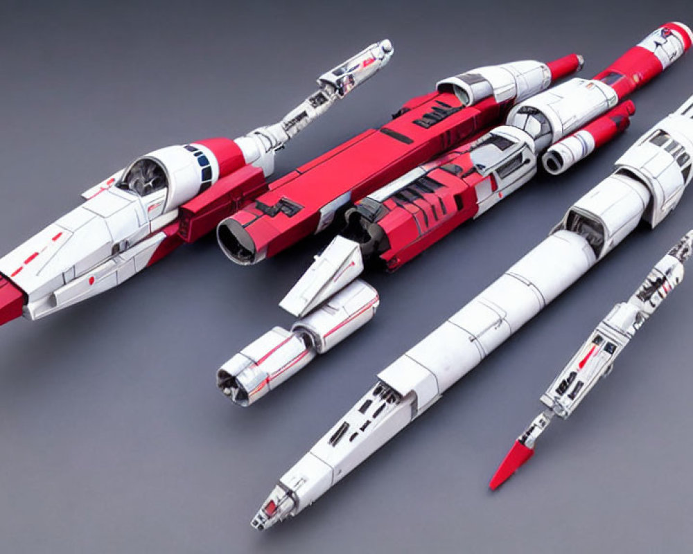 Three miniature spaceship models: red and white designs on grey surface