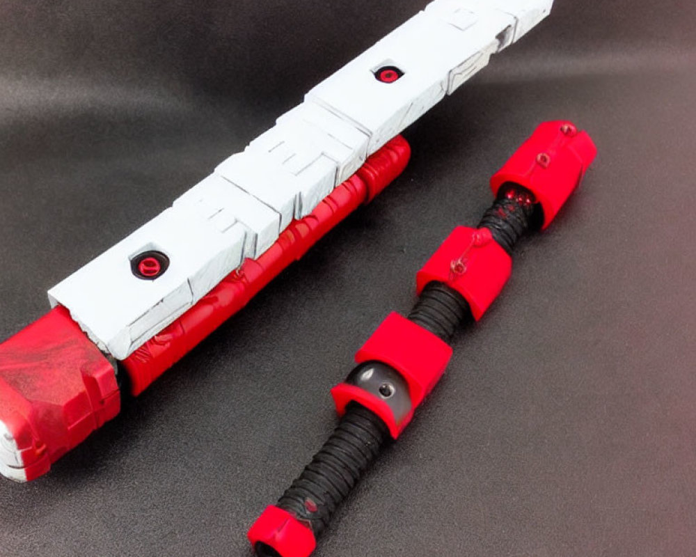 Red and White Sci-Fi Toy Swords with Black Grips on Black Surface