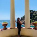 Person in dark dress between columns gazes at ocean view with cliffs and blue sky
