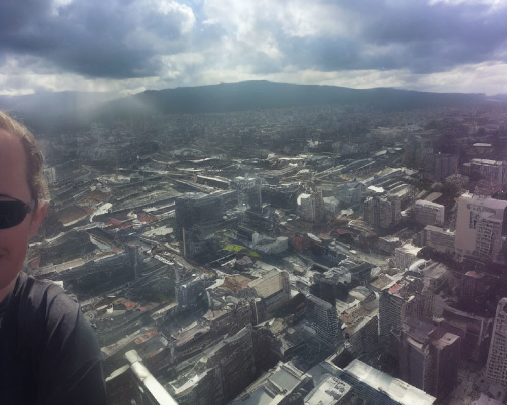 Cloudy cityscape with buildings, person's face, distant mountains, and sunlight.