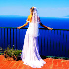 Bride in white wedding dress on terrace overlooking sea with bouquet