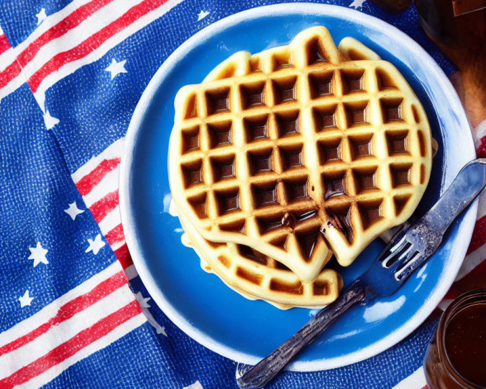 Heart-shaped waffle on blue plate with syrup on American flag-themed tablecloth