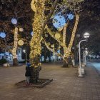 Person in Blue Jacket Under Tree with Twinkling Lights on Quaint Night Street