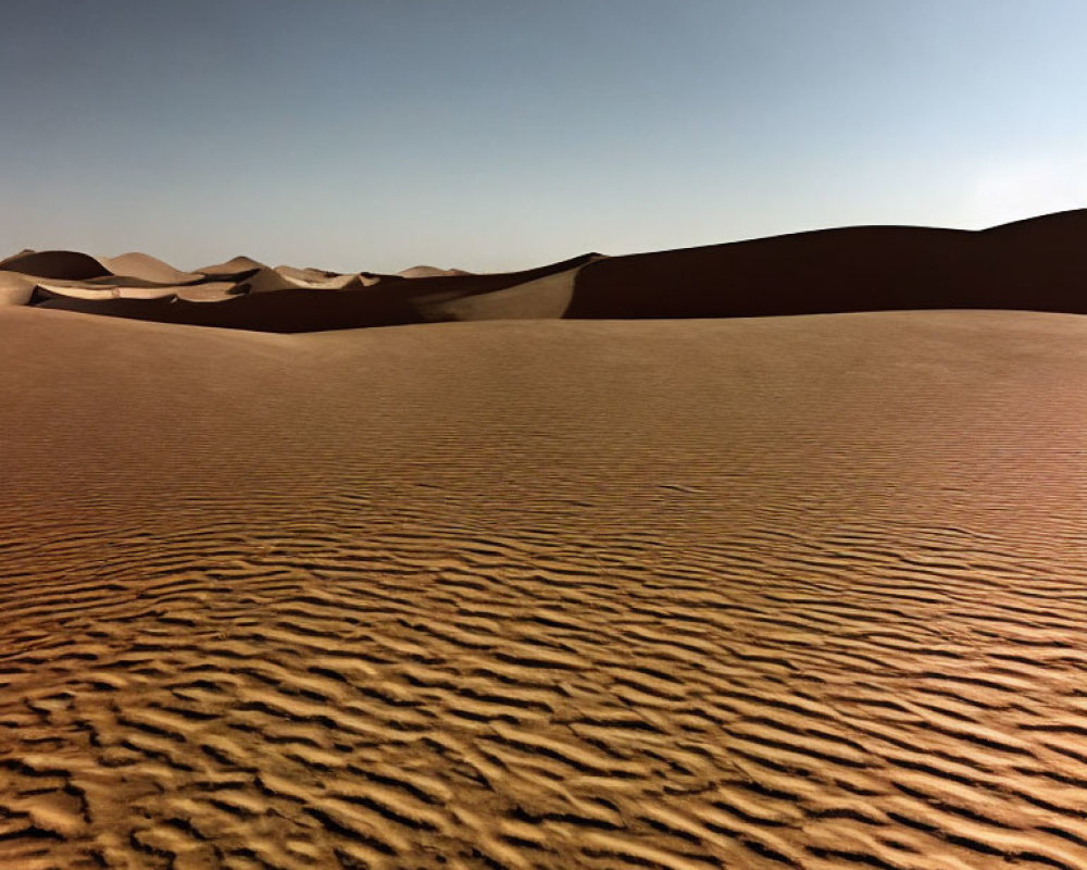 Desert landscape with rippled sand and smooth dunes under clear blue sky