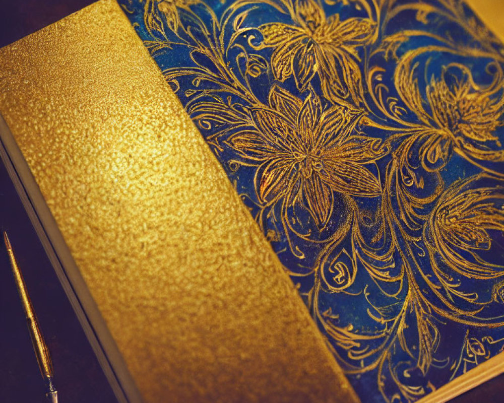 Blue and Gold Floral Pattern Journal with Golden Pen on Dark Surface