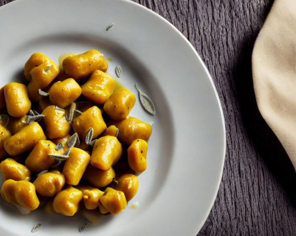 Seasoned Gnocchi on White Plate with Herbs and Napkin on Dark Wood