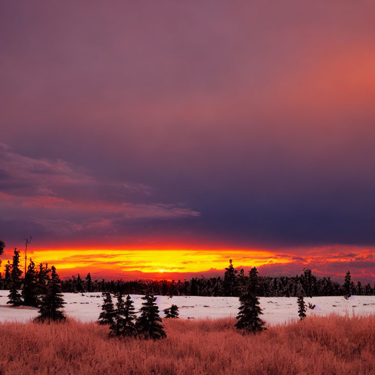 Vibrant orange and purple hues in fiery sunset over snow-covered landscape