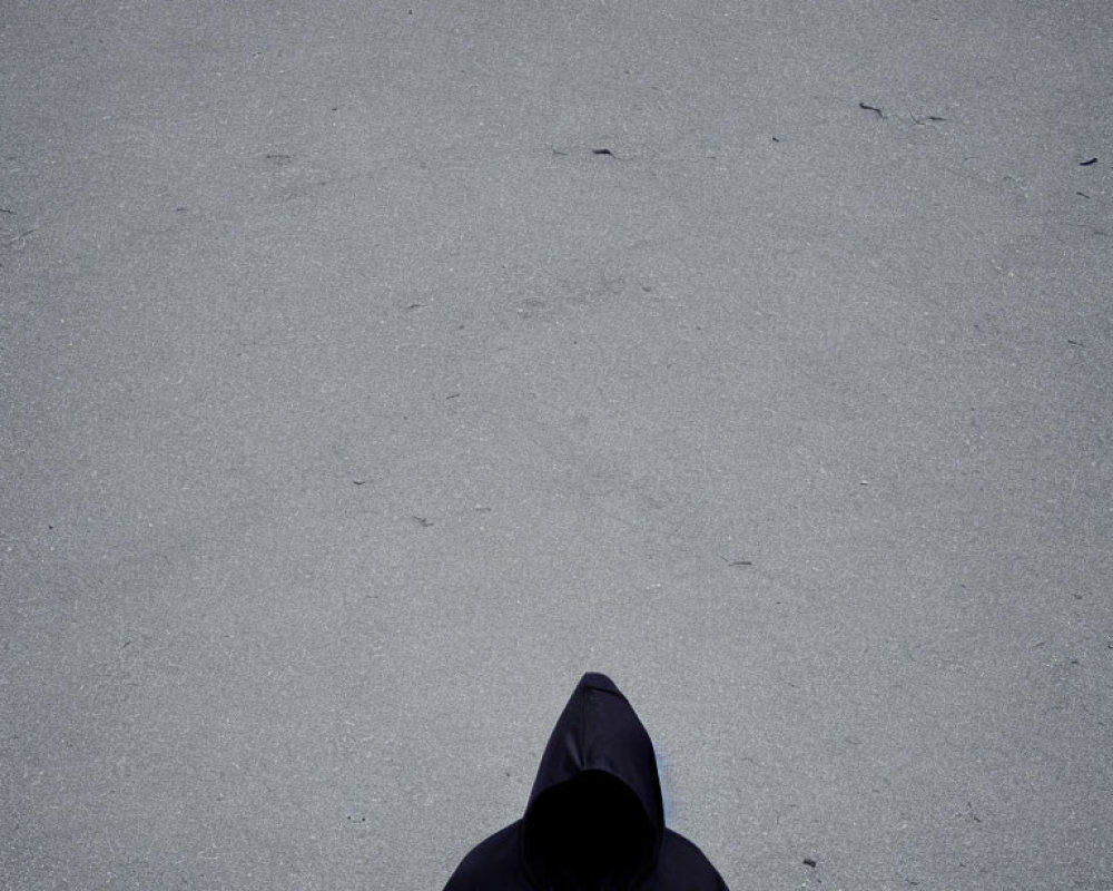 Hooded figure in jacket on grey asphalt.