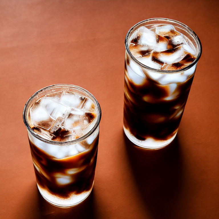 Iced coffee glasses with swirling milk on brown surface