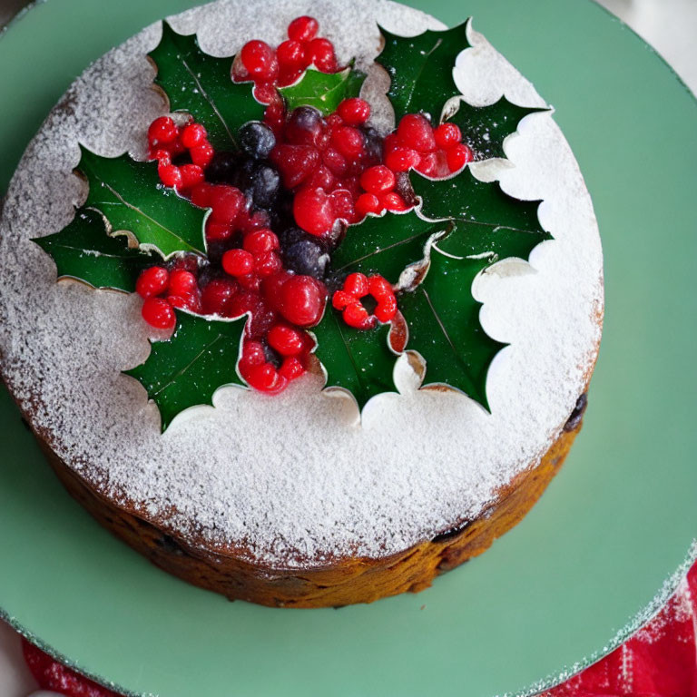 Festive fruitcake with holly leaves and berries on green plate