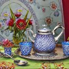 Floral-patterned tea set on green tablecloth with teapot, cups, and plate