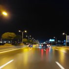 Urban night scene: glowing street lights, car light trails, illuminated signage.
