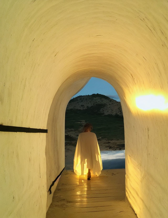 Figure in white cloak gazes at landscape from tunnel's end at dusk or dawn