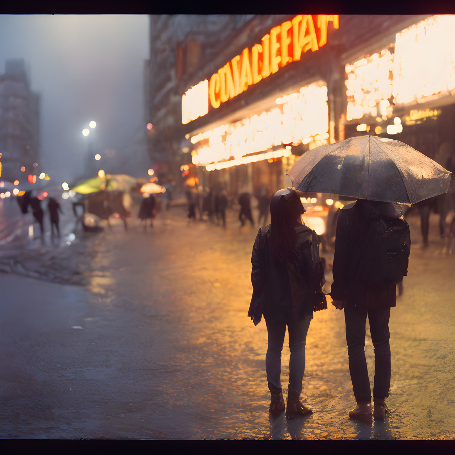 Two people sharing an umbrella in the rain under city lights