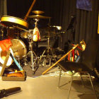 Drummer performing on stage with drum set and cables under warm lighting