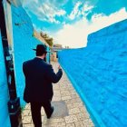 Man in suit and hat walking in vibrant blue alleyway under azure sky