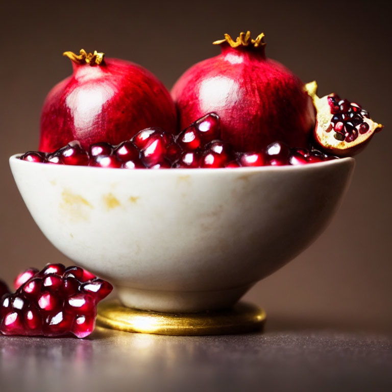 Fresh pomegranate seeds and whole fruit in bowl on blurred background