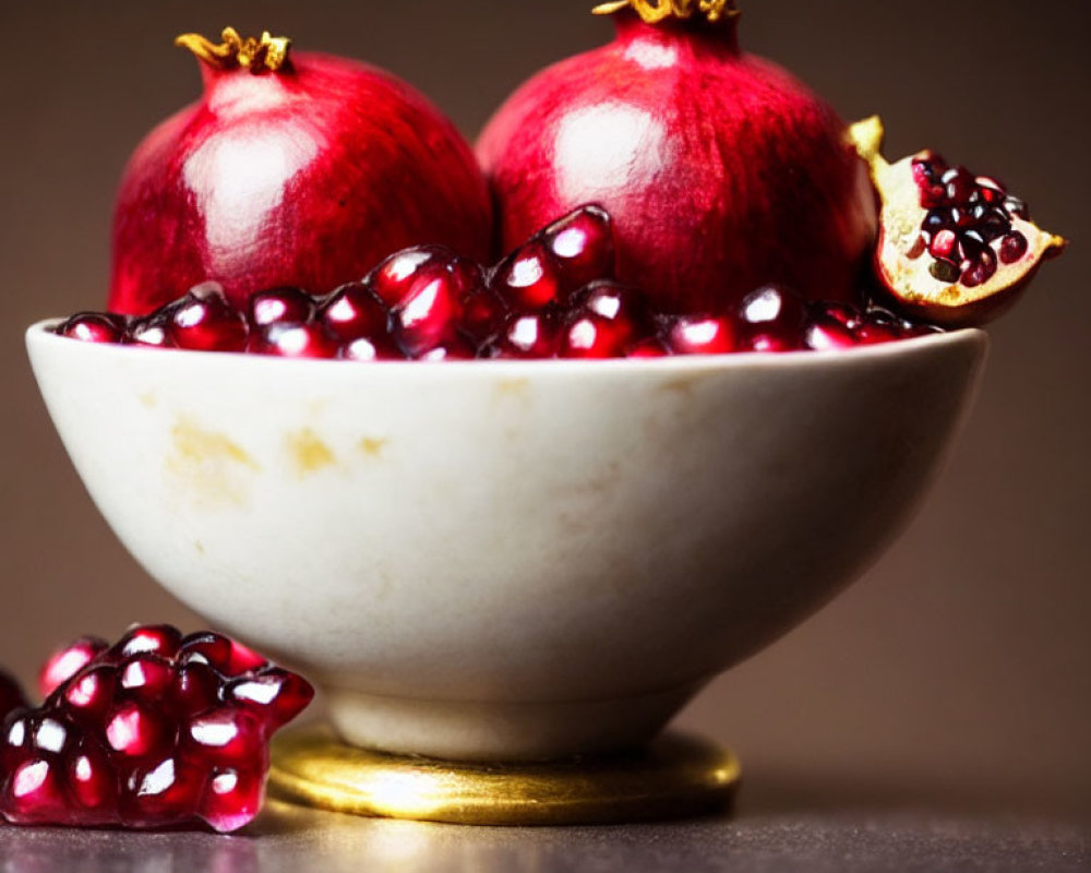 Fresh pomegranate seeds and whole fruit in bowl on blurred background