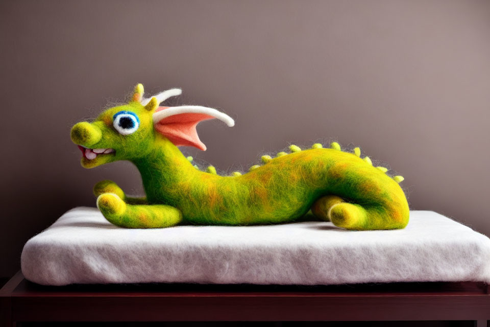 Colorful Felt Dragon with Big Eyes and Wings on Cushion and Wooden Surface