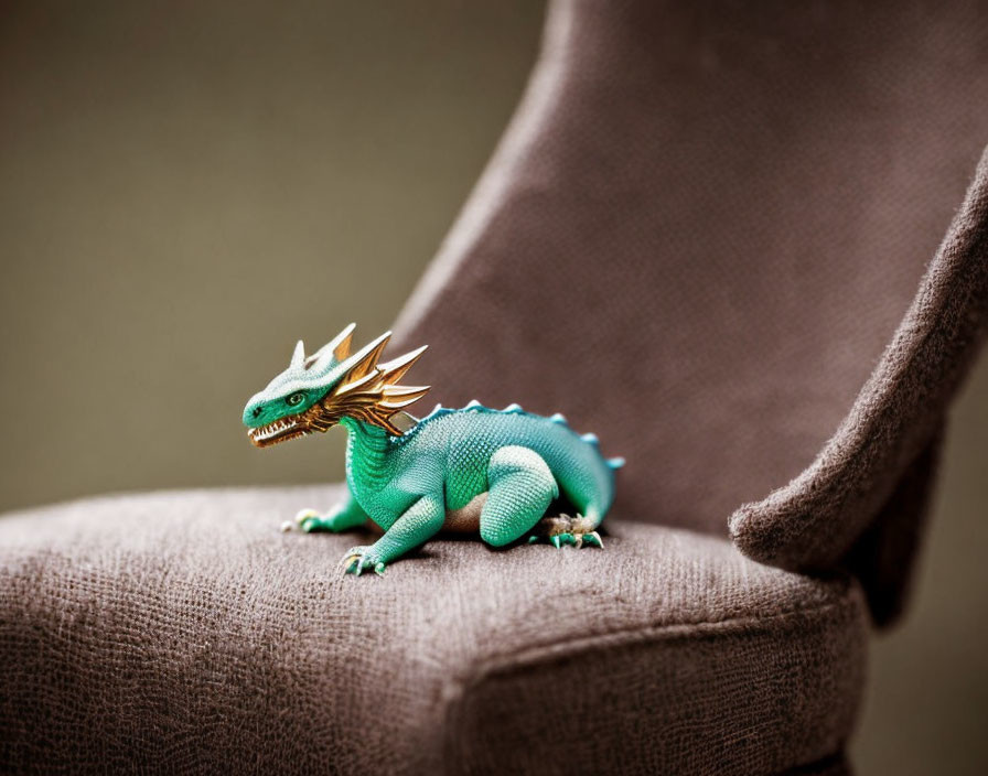 Blue and green toy dragon on grey chair armrest with blurred background