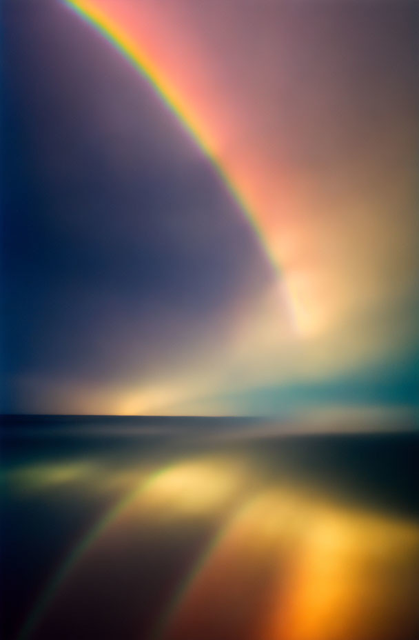 Vibrant rainbow over calm sea at sunset