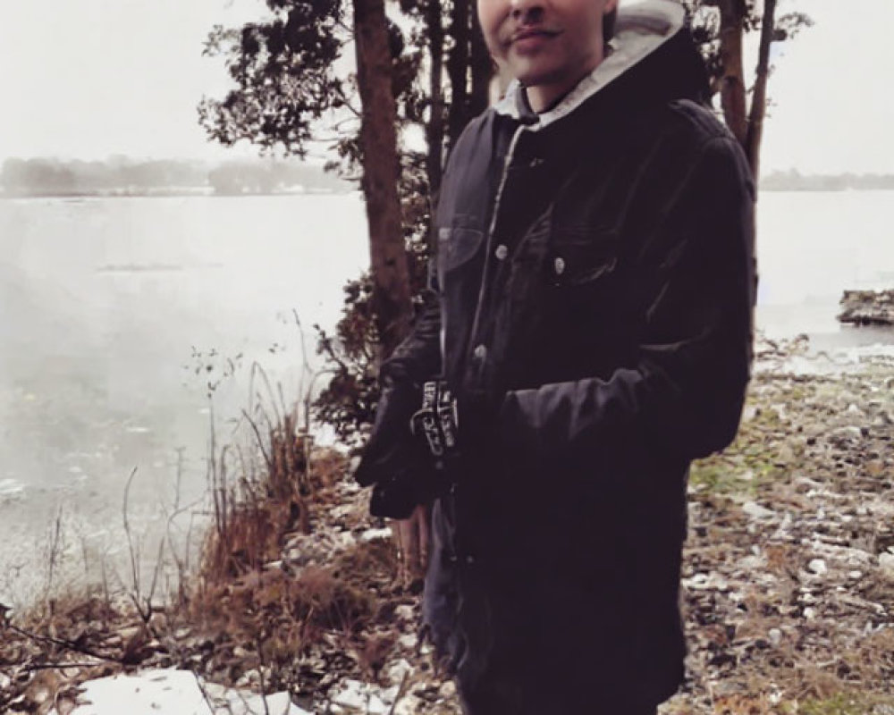Person in Winter Jacket by Snowy Lakeside with Trees and Overcast Skies