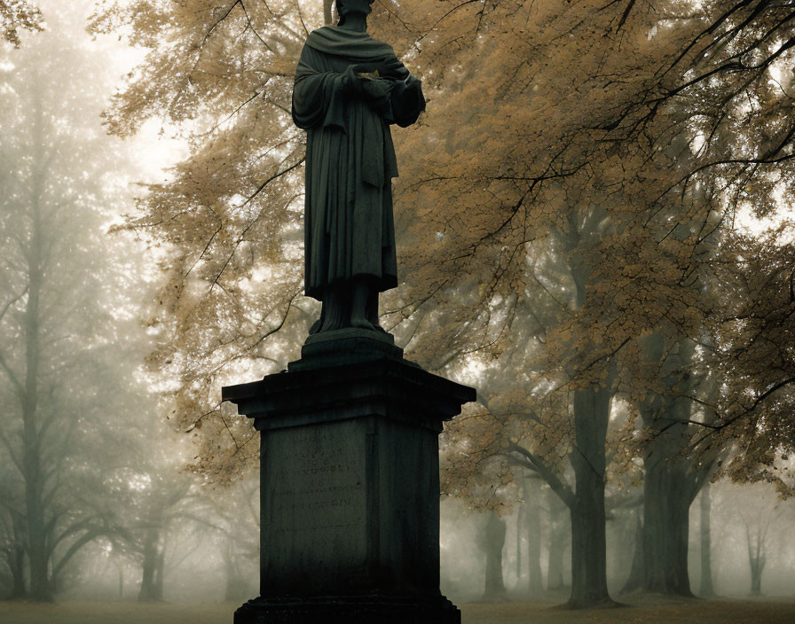 Misty park with solemn statue and autumnal trees.